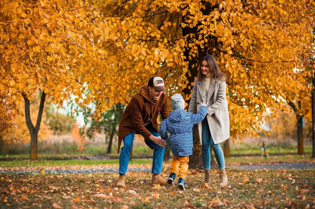 mom and dad with child around fall trees